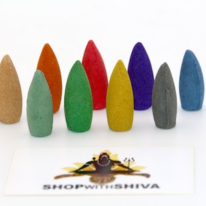 May include: Assortment of ten backflow incense cones in various colours, including beige, green, orange, red, yellow, blue, purple, and grey. The cones are arranged in a row on a white surface. The cones are made of a textured material and have a pointed tip. The cones are labelled "SHOPWITHSHIVA".
