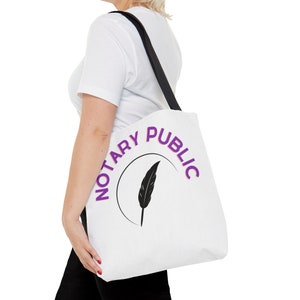 May include: White tote bag with a purple circle and the text "Notary Public" around the circle. Inside the circle is a black feather quill.