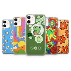 May include: Five different phone cases with various designs. The cases are all clear and show the phone's camera lens. The designs include daisies, a rainbow, a green frog, a rainbow with a strawberry, and orange flowers.