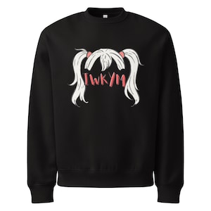 Puede incluir: Sudadera negra con un gráfico de pelo blanco en coletas atadas con cintas rosas. El texto rosa "I WKYM" está debajo. La sudadera tiene cuello redondo y mangas largas.