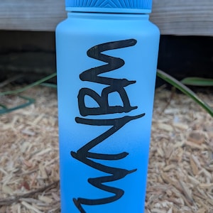 Puede incluir: Una botella de agua con degradado de azul claro a azul brillante con acabado mate y tapa azul claro a juego con asa de transporte. El lateral de la botella muestra el texto negro "RUNBM" escrito en una fuente negrita de estilo manuscrito.