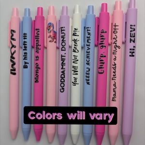 Puede incluir: Un conjunto de nueve bol&iacute;grafos retr&aacute;ctiles en tonos pastel rosa, azul, blanco y lavanda. Cada bol&iacute;grafo tiene texto impreso en negro, incluyendo frases como "IWKYM", "By his left tit", "Mongo is appalled", "GODDAMNIT, DONUT!", "You Will Not Break Me", "NEEEW ACHIEVEMENT!", "Glurp, glurp", "Mama Needs a Night Off", "HI, ZEVI!" y uno con un gr&aacute;fico de dinosaurio.