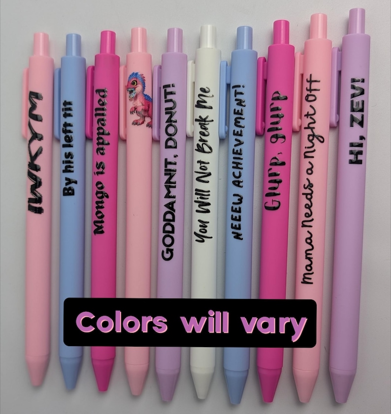 Puede incluir: Un conjunto de nueve bol&iacute;grafos retr&aacute;ctiles en tonos pastel rosa, azul, blanco y lavanda. Cada bol&iacute;grafo tiene texto impreso en negro, incluyendo frases como "IWKYM", "By his left tit", "Mongo is appalled", "GODDAMNIT, DONUT!", "You Will Not Break Me", "NEEEW ACHIEVEMENT!", "Glurp, glurp", "Mama Needs a Night Off", "HI, ZEVI!" y uno con un gr&aacute;fico de dinosaurio.