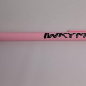 Puede incluir: Un bol&iacute;grafo retr&aacute;ctil de color rosa claro con acabado mate y clip de bolsillo. El texto IWKYM est&aacute; impreso en letras may&uacute;sculas negras y negritas a lo largo del cuerpo del bol&iacute;grafo, colocado horizontalmente cerca del extremo superior.