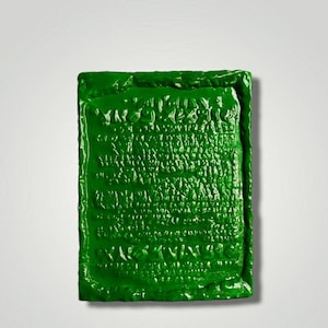 Op de afbeelding: Een groene keramische plaquette met een reli&euml;f, getextureerd oppervlak. De plaquette heeft een ontwerp van een herhalend patroon van letters en symbolen.
