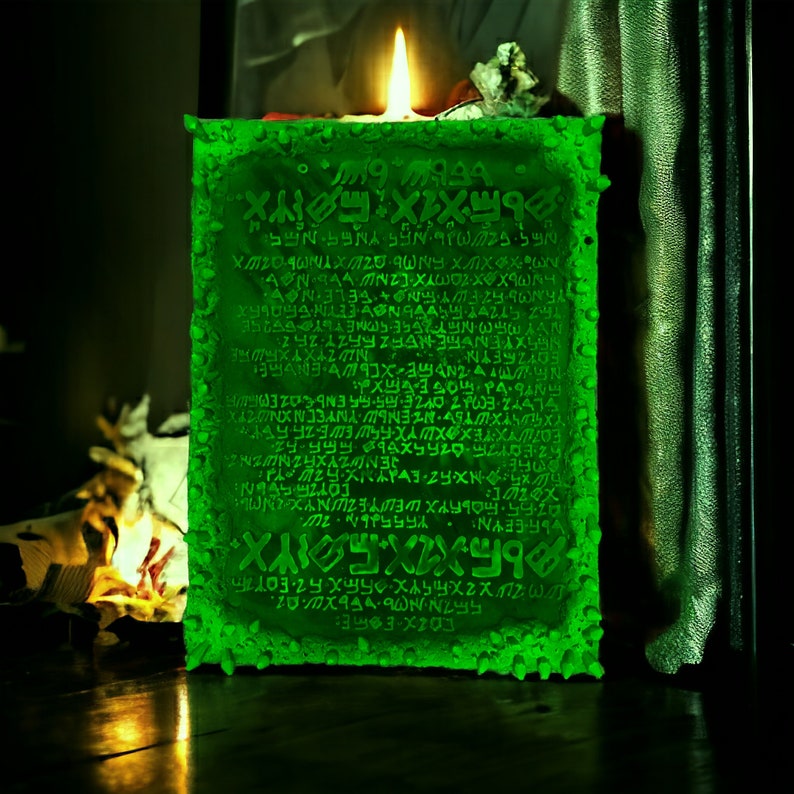 May include: A glowing green candle with ancient-looking text carved into its surface. The candle is rectangular with a textured, uneven edge. A lit flame sits atop the candle, casting a warm glow. The background is dark.