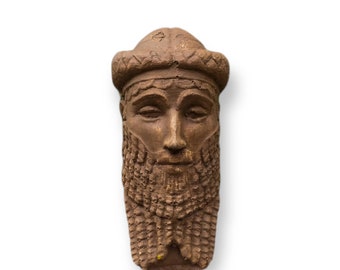May include: A terracotta sculpture of a bearded man's head wearing a crown. The sculpture is brown and has a detailed design.