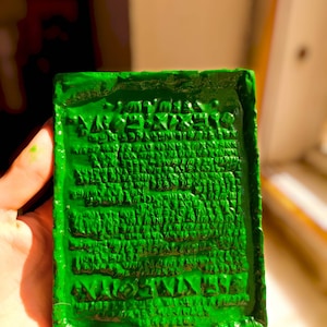 Op de afbeelding: Een groene rechthoekige blok met een verhoogde inscriptie in een oude taal. De inscriptie is in een schrift dat lijkt op spijkerschrift.