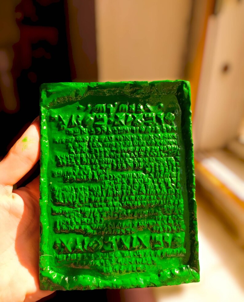 Op de afbeelding: Een groene rechthoekige blok met een verhoogde inscriptie in een oude taal. De inscriptie is in een schrift dat lijkt op spijkerschrift.