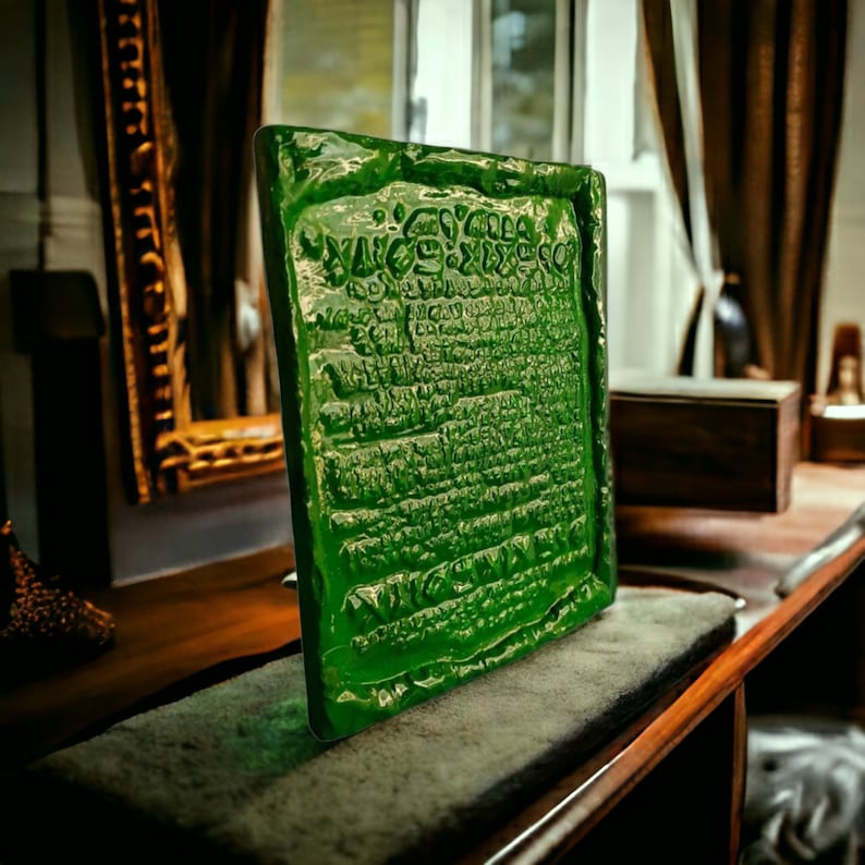 Op de afbeelding: Een groene glazen plaquette met een inscriptie in een oude taal. De plaquette ligt op een houten oppervlak.