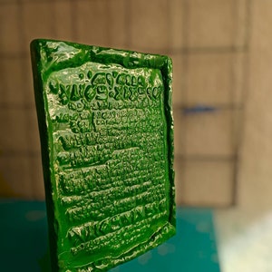 Op de afbeelding: Een groene rechthoekige plaquette met reli&euml;fletters. De letters zijn in een oude taal en bevatten het woord "VICTORY".