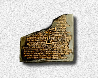 May include: A fragment of a stone tablet with a cross carved into it. The tablet is covered in text written in an old script. The text is in gold and the stone is dark brown.