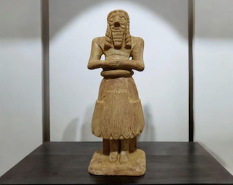 May include: A terracotta sculpture of a standing figure with a beard and a long skirt. The figure has its arms crossed in front of its chest.