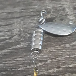 May include: A silver fishing lure with a single treble hook. The lure has a silver body with a ribbed design and a silver blade.