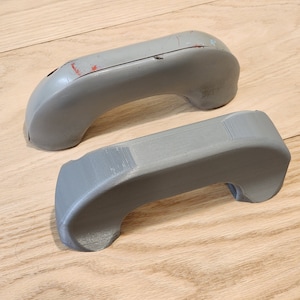 May include: Two gray plastic door handles. The top handle has some wear and tear.