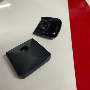 May include: Two black plastic door handles. One is a square shape with a round hole in the center. The other is a curved shape with a round hole in the center.
