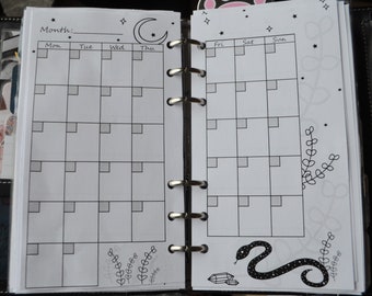 Peut inclure: Un agenda noir et blanc avec une mise en page de calendrier mensuel. Le calendrier présente un design de croissant de lune et d'étoiles. L'agenda a un design de serpent noir et de cristal sur la page de droite.