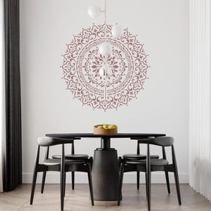 Könnte beinhalten: Ein schwarzer Esstisch mit vier schwarzen Stühlen und einem rosafarbenen Mandala-Design an der Wand dahinter. Der Tisch hat eine runde Tischplatte und ein zylindrisches Gestell. Die Stühle haben eine geschwungene Rückenlehne und einen Holz-Sitz. Das Mandala-Design ist kompliziert und detailliert.