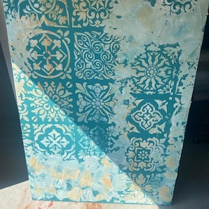 Może przedstawiać: Turkusowe płótno z białym i złotym wzorem malarskim. Wzór przedstawia powtarzający się wzór geometrycznych kształtów i motywów kwiatowych.