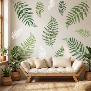 Könnte beinhalten: Ein Wohnzimmer mit einem hellen Sofa, beigen Kissen und einem Holzrahmen. Die Wand ist mit Farnblatt-Aufklebern in Grün und Weiß verziert. Topfpflanzen und ein gewebter Teppich vervollständigen die natürliche Ästhetik.