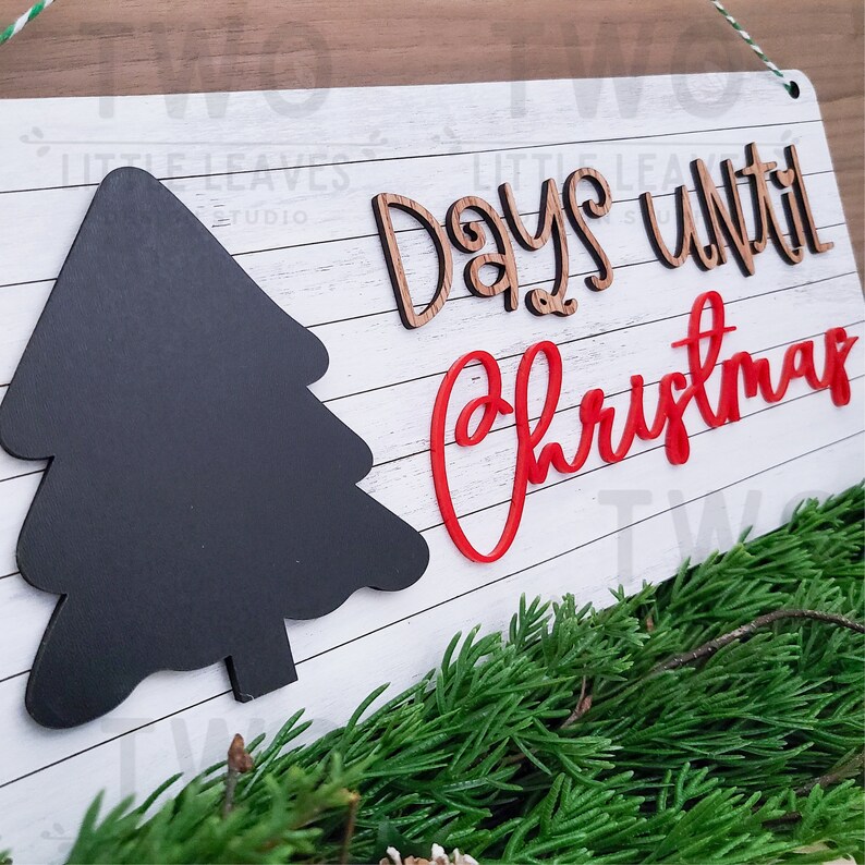 May include: White wooden sign with a black chalkboard tree and the words "Days until Christmas" in brown and red lettering.