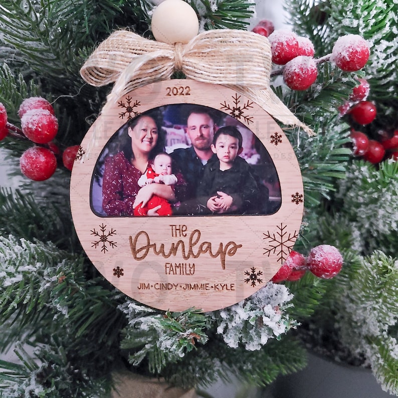 K&ouml;nnte beinhalten: Ein runder Weihnachtsbaumschmuck aus Holz mit einem Foto einer vierk&ouml;pfigen Familie. Der Schmuck ist mit Schneeflocken und dem Text "The Dunlap Family" und "Jim-Cindy-Jimmie-Kyle" verziert. Das Jahr 2022 ist ebenfalls auf dem Schmuckst&uuml;ck enthalten.