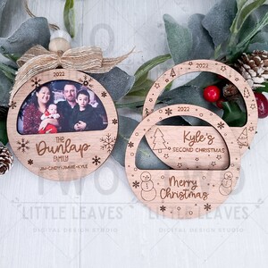 K&ouml;nnte beinhalten: Zwei h&ouml;lzerne Weihnachtsbaumschmuckst&uuml;cke mit einem Fotorahmen und einem Schneemann-Design. Das erste Ornament hat ein Familienfoto mit dem Text "The Dunlap Family" und "JIM-CINDY-JIMMIE-KYLE". Das zweite Ornament hat den Text "Kyle's Second Christmas" und "Merry Christmas".