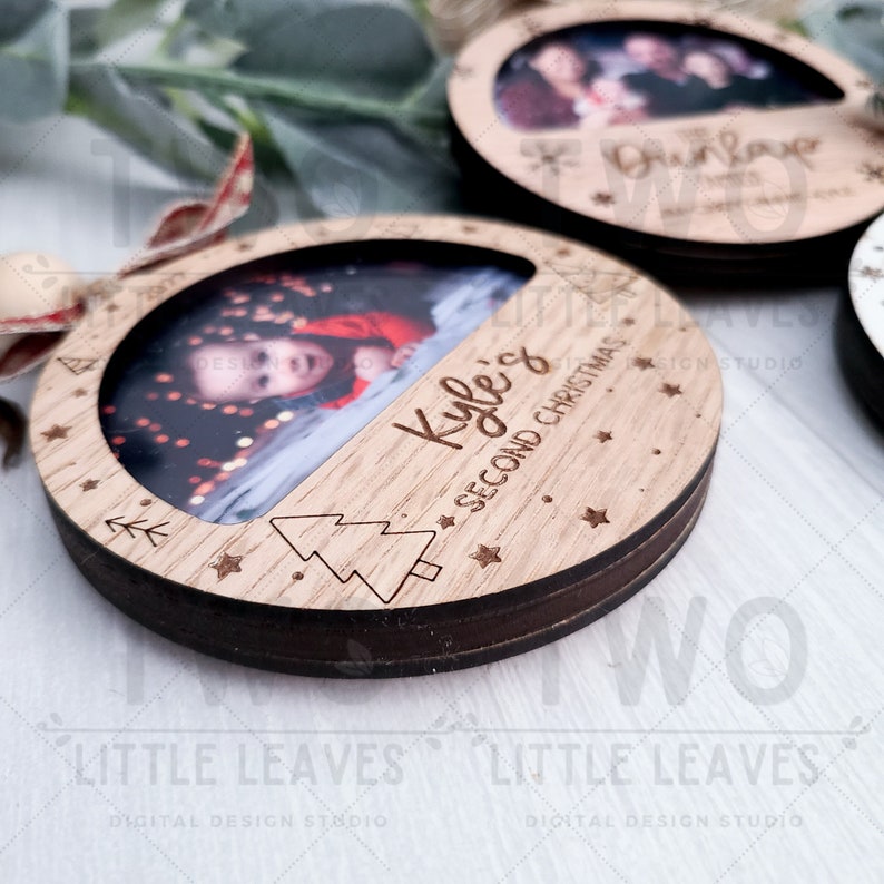 K&ouml;nnte beinhalten: Ein Weihnachtsbaumschmuck aus Holz mit einem Foto eines Kindes in einem roten Shirt. Der Schmuck ist mit dem Text "Kyle's Second Christmas" graviert und hat einen kleinen Baum und Sterne um das Foto herum.