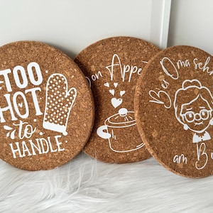 Könnte beinhalten: Drei Korkuntersetzer mit weißem Text und Designs. Der erste Untersetzer sagt "Too Hot to Handle" mit einem weißen Ofenhandschuh. Der zweite Untersetzer sagt "Bon Appetit" mit einem weißen Topf und Herzen. Der dritte Untersetzer sagt "Bei Oma schmeckt's am Besten" mit einer weißen Illustration einer Großmutter.
