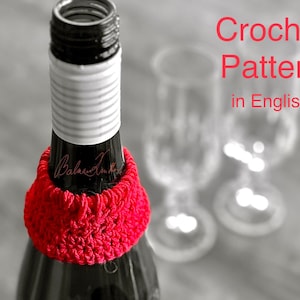 May include: A vibrant red crocheted wine bottle cosy encircles a dark wine bottle. The text "Crochet Pattern in English" is displayed in red. The background is blurred, with two wine glasses visible.
