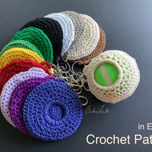 May include: A collection of crocheted keychains in various colors, including red, yellow, green, purple, and blue. The keychains are arranged in a circle, with a crocheted tennis ball keychain in the center. The keychains are all attached to a silver key ring. The image includes the text "in English Crochet Pattern".