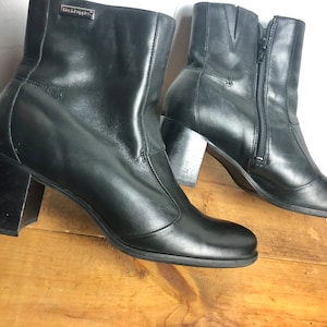 Könnte beinhalten: Paar schwarze Leder-Stiefeletten mit Blockabsatz und seitlichem Reißverschluss. Die Stiefeletten haben eine spitze Zehenpartie und ein kleines Logo an der Seite.