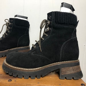 May include: Black suede ankle boots with a chunky platform sole and a brown rubber outsole. The boots have a lace-up closure and a knitted cuff around the ankle.