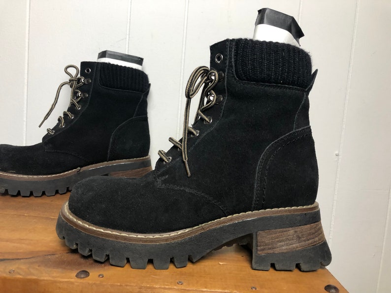 May include: Black suede ankle boots with a chunky platform sole and a brown rubber outsole. The boots have a lace-up closure and a knitted cuff around the ankle.