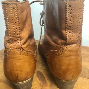 May include: A pair of brown leather ankle boots with laces. The boots have a brogue design and a low heel.