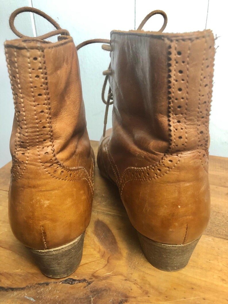 May include: A pair of brown leather ankle boots with laces. The boots have a brogue design and a low heel.