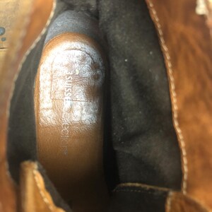 May include: Close-up of the inside of a brown leather boot with a black fabric lining. The insole is brown and has the text "JustFab" printed on it.