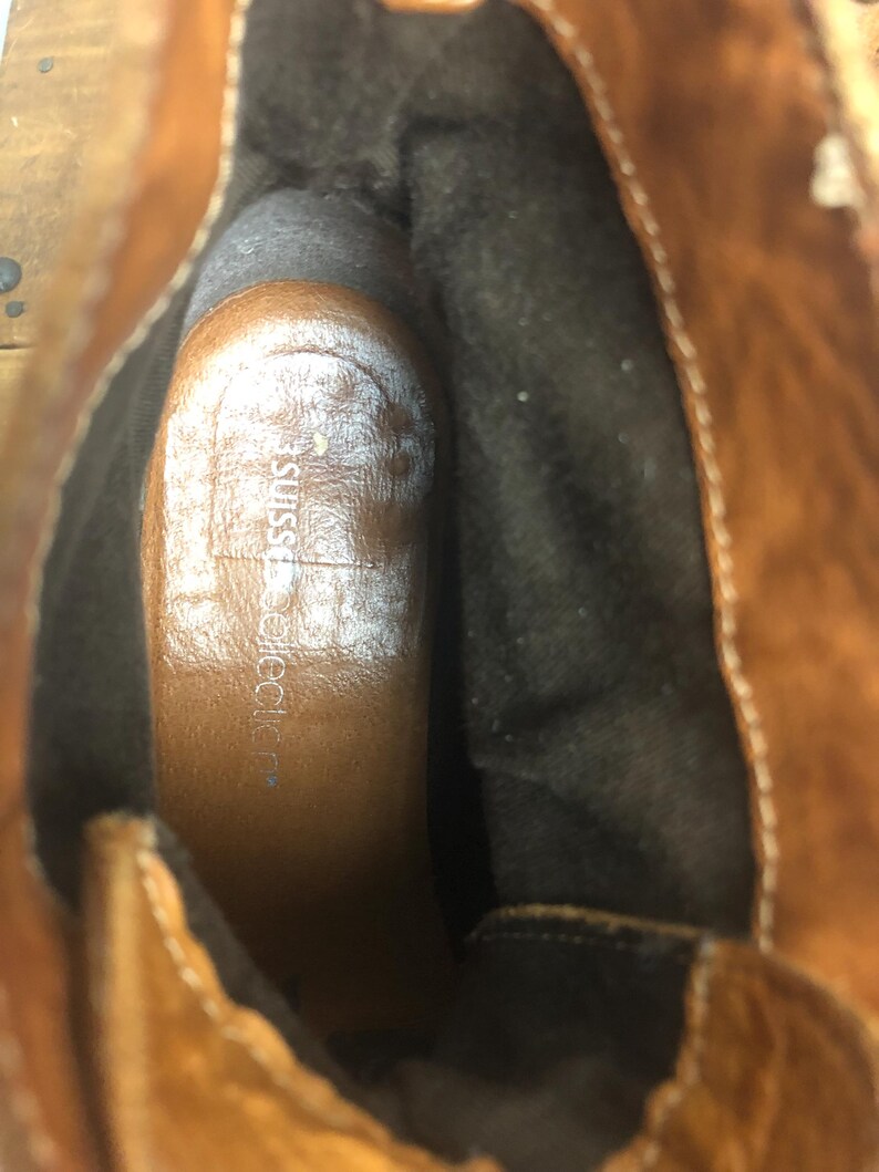 May include: Close-up of the inside of a brown leather boot with a black fabric lining. The insole is brown and has the text "JustFab" printed on it.