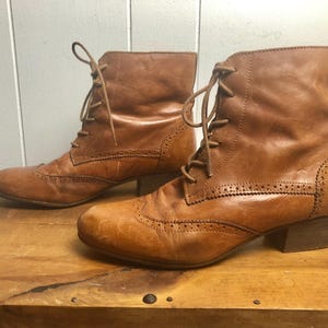 May include: A pair of brown leather ankle boots with lace-up closures and a brogue design. The boots have a low block heel.
