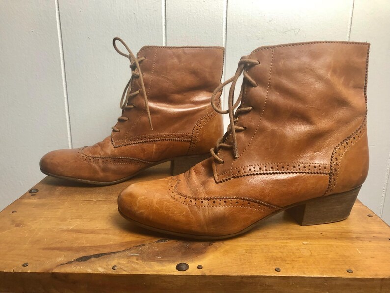 May include: A pair of brown leather ankle boots with lace-up closures and a brogue design. The boots have a low block heel.