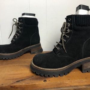 May include: A pair of black suede lace-up boots with chunky platform soles. The boots have a brown rubber outsole and a black knit cuff around the ankle.