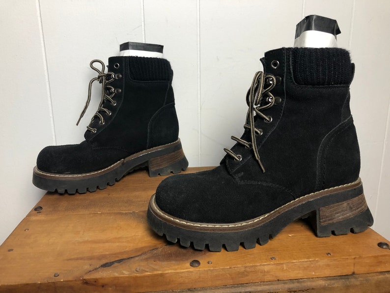 May include: A pair of black suede lace-up boots with chunky platform soles. The boots have a brown rubber outsole and a black knit cuff around the ankle.