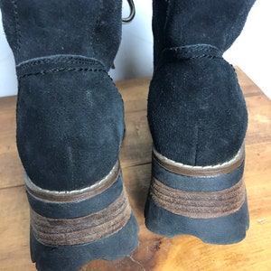 May include: A pair of black suede boots with brown rubber soles. The boots have a lace-up front and a chunky heel.