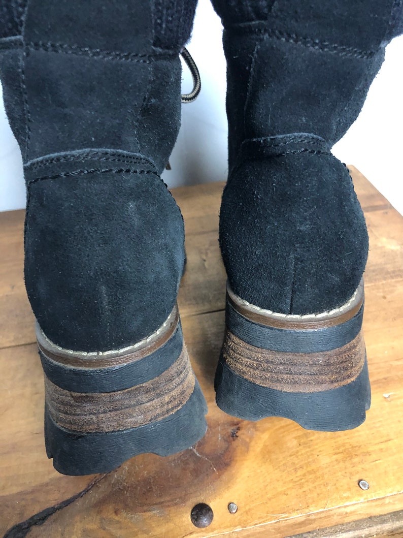 May include: A pair of black suede boots with brown rubber soles. The boots have a lace-up front and a chunky heel.