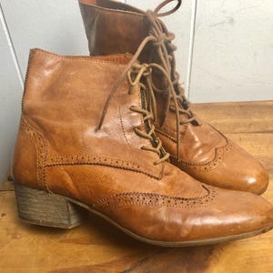 May include: A pair of brown leather ankle boots with lace-up closures and a brogue design. The boots have a low block heel.