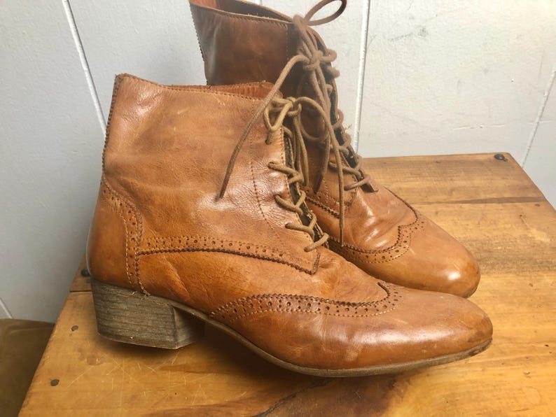 May include: A pair of brown leather ankle boots with lace-up closures and a brogue design. The boots have a low block heel.