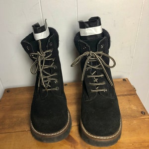 May include: A pair of black suede lace-up boots with a thick sole and a brown trim around the edge.