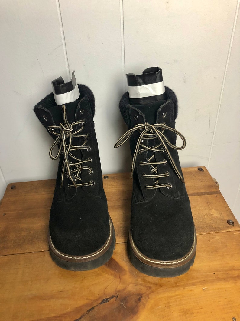 May include: A pair of black suede lace-up boots with a thick sole and a brown trim around the edge.