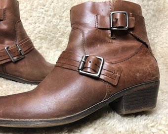 May include: Brown leather ankle boots with double buckle straps and a low block heel.