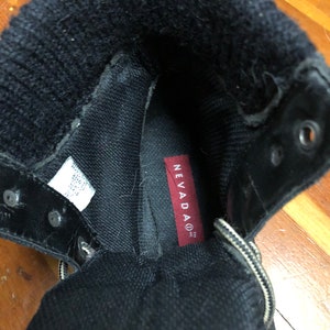 May include: Close-up of the inside of a black boot with a red label that says "NEVADAO TM INC".